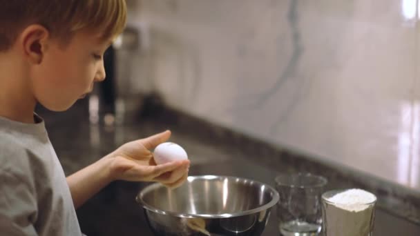 孩子拿起一个鸡蛋 把它打碎成一个铁碗 用来揉碎面团 一个8岁的白人男孩在厨房里做饭 吃饭时间 童年的幸福 — 图库视频影像