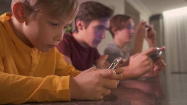 自宅でスマートフォンを持つ子供たち 3人の男の子が携帯電話を使ってソーシャルネットワークで時間を過ごしています ゲームに携帯電話を使う白人の子供 ライフスタイルの概念 フルHdリアルタイム映像 — ストック動画