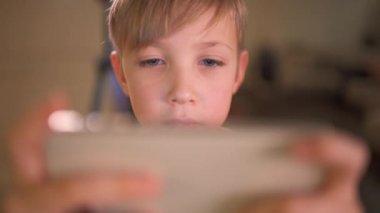 Evinde akıllı telefonlu bir çocuğun yüzünü kapat. Beyaz bir çocuk sosyal ağda cep telefonu kullanarak zaman geçiriyor. Beyaz çocuk oyun için cep telefonu kullanıyor. Yaşam tarzı konsepti. Tam HD görüntü.   