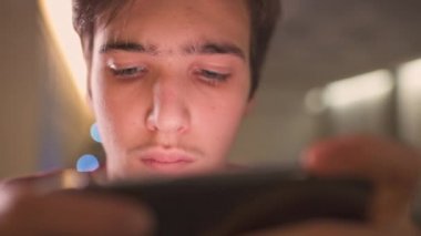 Evde akıllı telefonlu bir gencin yüzünü kapat. Kafkasyalı genç adam sosyal ağda cep telefonu kullanarak zaman geçiriyor. Beyaz genç adam oyun için cep telefonu kullanıyor. Yaşam tarzı kavramı. 