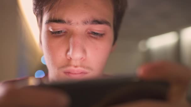 Visage rapproché d'un adolescent avec smartphone, à la maison. Caucasien adolescent gars passer du temps dans un réseau social en utilisant le téléphone mobile. Jeune homme blanc utilisant un téléphone portable pour jouer. Concept de style de vie. 