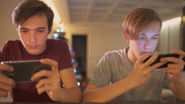 自宅でスマートフォンを持つ10代の男の子 2人の男の子は携帯電話を使ってソーシャルネットワークで時間を過ごしています ゲームに携帯電話を使う白人のティーンエイジャー クローズアップビューを持つ若者 — ストック動画