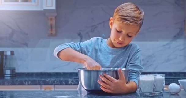 スローモーション4K映像 キッチンでの少年料理 白い少年はクッキーの生地を攪拌 子供はスチールボウルにケーキのための成分を混合しています 家庭で料理をする8歳の子供 — ストック動画