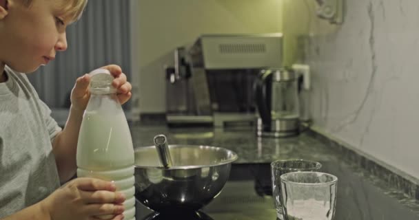 子供は牛乳を1本持って鉄のボウルに注ぎます 8歳の白人の少年が台所で料理をする 食事の時間だ 幼少期の概念 4Kスローモーション映像 — ストック動画