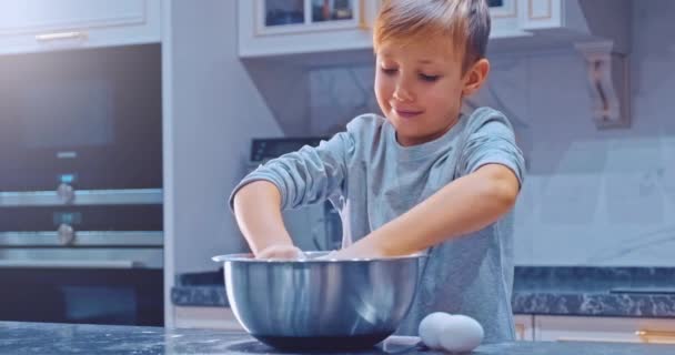 スローモーション4K映像 キッチンでの少年料理 白い少年がクッキーのために手で生地を攪拌 子供はスチールボウルにケーキのための成分を混合しています 8歳の子供が家庭で料理をする — ストック動画