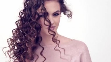 Uzun kıvırcık saçlı güzel bir kadın. Güzel surat. Moda modeli. Moda makyajı. Göz makyajlı çekici bir kız. Bir kızın yakın çekim yüzü. Yavaş çekim 4K görüntüsü. Seksi esmer bayan..  
