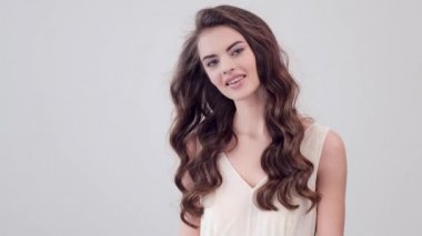 Uzun kıvırcık kahverengi saçlı, gülümseyen güzel bir kadın. Moda modeli stüdyodaki kameraya bakıyor. Çekici esmer bir kadının yakın çekim yüzü. Saexy görünüşlü seksi bir manken. 4K görüntü. Yavaş çekim. 
