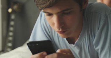Ergen, akıllı telefonuyla evde mesaj yazıyor. Çekyatta uzanmış cep telefonu kullanarak sosyal ağda vakit geçiren yakışıklı çocuk. Kafkasyalı genç adam cep telefonuyla konuşuyor. Yaşam tarzı kavramı.