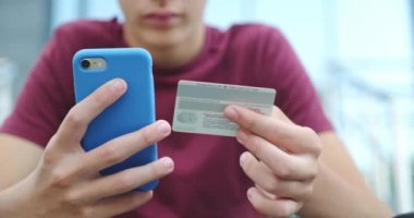 İnsanlar açık havada, kredi kartı ve cep telefonu kullanarak online alım yapıyorlar. İnsan eli cep telefonunu banka kartıyla tutuyor. Erkek eller online alışveriş için akıllı telefon ve kredi kartı kullanır. Yakın çekim..