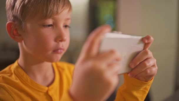 在家里 一个拿着智能手机的男孩的近视 白人儿童用手机在社交网络中度过时光 白人小孩用手机玩游戏生活方式概念 — 图库视频影像