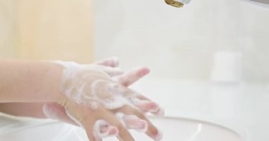 Çocuğun elleri deriyi yıkamak için ellerini köpükle lavaboda yıkar. Su ellerden akar. Mikropların ve koronavirüsün ellerle temas etmesini engelliyor ve temizliyor
