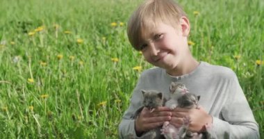 Ağır çekimde - Çocuk küçük kedi yavrularını elinde tutuyor. Ellerinde kedi yavrusu olan mutlu çocuk çimlerin üzerinde oturuyor. Sevimli bebek elinde üç evcil hayvanla çimlerin üzerinde oturuyor..  