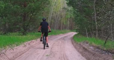  Orman yolunda bisiklete binen genç adama arka manzara. Yazın MTB bisikleti süren bisiklet kasklı bir adam. Dağ bisikleti süren bir genç ormanda geziyor. Gerçek zamanlı görüntüler