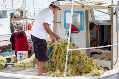 Yaşlı bir balıkçı teknesindeki balık ağlarını tamir etmekle meşgul..