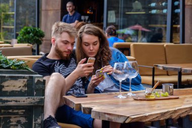 Bir erkek ve bir kız, sosyal ağlardaki izlenimlerini bir kafenin verandasında paylaşıyorlar. .