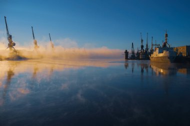 Nehrin ayna yüzeyinden, seti gizleyen sis yükselir, alçak güneş iskele vincinin ve demirli geminin oklarını aydınlatır..