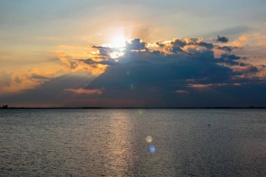 Denizde gün batımı, güneş ışınları ağır bulutların arasından yol alır..