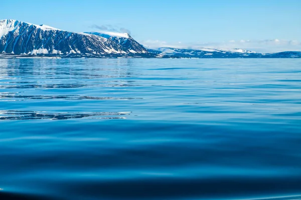 Una vista de la isla ártica desde el mar, más allá del océano, se puede ver la orilla, las montañas cubiertas de nieve y el glaciar deslizándose en el agua, el Ártico . — Foto de Stock