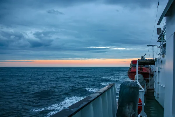 Before the storm sunset at sea, a view of the stern of the deck of a scientific vessel, on the horizon a strip without a clastic orange sky.