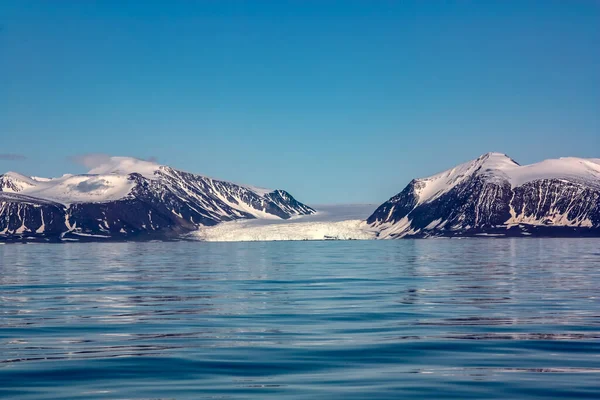 Una vista de la isla ártica desde el mar, más allá del océano, se puede ver la orilla, las montañas cubiertas de nieve y el glaciar deslizándose en el agua, el Ártico . — Foto de Stock