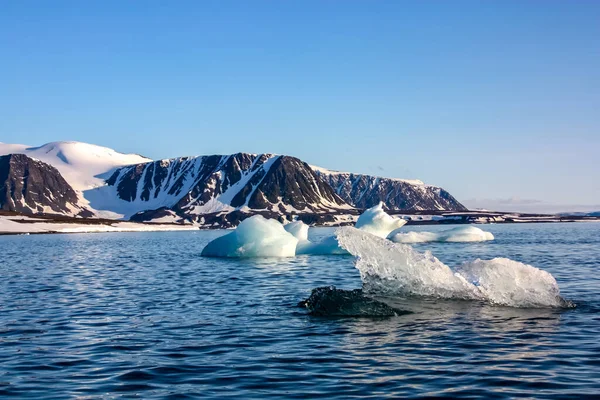 En utsikt över den arktiska ön från havet, bortom havet, kan du se stranden, bergen täckta med snö och på vattenytan små isberg, den arktiska. — Stockfoto