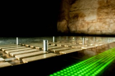 Birçok altın külçesi yeşil LED ışık çubuğu olan güvenli ve güçlü bir odanın karanlığında saklanır.