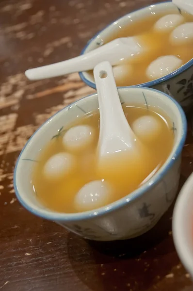 Many bowls of famous hot and cold sweet dessert soup in a round table with her friend in Hong Kong restaurant cafe. There are black sesame soft silky balls in hot soup