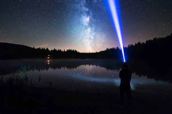 Yıldızlı gece gökyüzünün altında duran adam, kafa lambasıyla parlıyor.