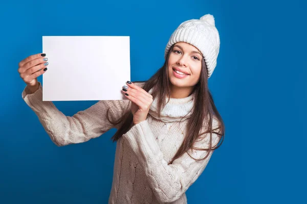 Your text here. Pretty young happy woman in winter clothes holding empty blank board. Colorful studio portrait with blue background. Christmas, x-mas, people, happiness concept