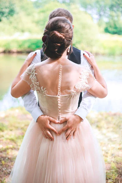 Gros plan de couple faisant forme de coeur avec les mains. Couple de mariage sur la nature se serre dans ses bras. Belle fille modèle en robe blanche. Un homme en costume. Mariée beauté avec marié . — Photo