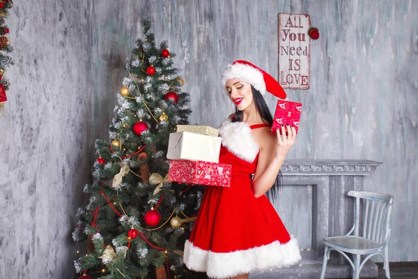 산타 클로스 옷을 입고 아름 다운 섹시 한 여자입니다. 크고 작은 선물 함께 웃는 여자. 여자 드레스와 산타의 모자에. 산타의 도우미 — 스톡 사진