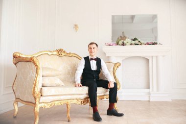  Damat kanepede onun düğününde gelin için bekleyen oturuyor. gülümseyen ve gelin için bekleyen düğün smokin. Zarif adam siyah kostüm ve papyon. 