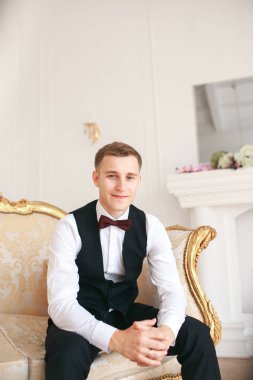  Damat kanepede onun düğününde gelin için bekleyen oturuyor. gülümseyen ve gelin için bekleyen düğün smokin. Zarif adam siyah kostüm ve papyon. 