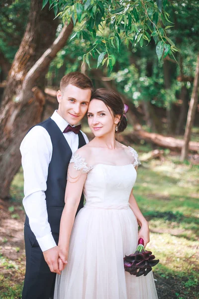 O noivo e a noiva juntos. abraços de casal. Dia do casamento. Bela noiva e elegante noivo andando após a cerimônia de casamento. Vestido de noiva de luxo e buquê de flores . — Fotografia de Stock