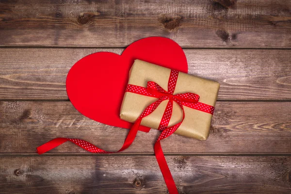 Wrapped vintage gift box with red ribbon bow and red heart on wooden background — Stock Photo, Image