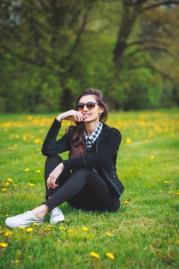 şık genç kız bir ekose gömlek ve ilkbaharda yeşil çimenlerin üzerinde oturan güneş gözlüğü