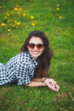 şık genç kız bir ekose gömlek ve güneş gözlüğü ilkbaharda yeşil çim üzerinde yalan