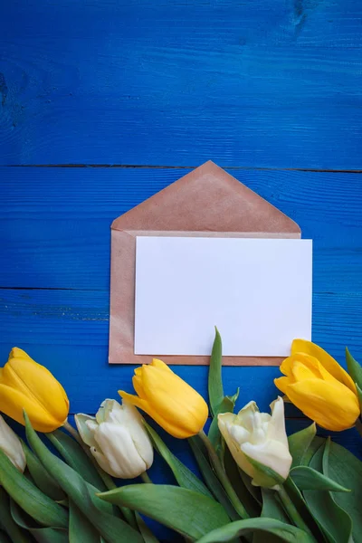 Flores de tulipa de primavera, cartão de papel presente na mesa de madeira azul de cima em estilo leigo plano. Saudação para o Dia da Mulher ou da Mãe . — Fotografia de Stock