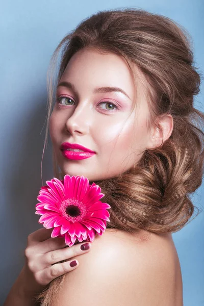 Портрет романтической молодой женщины с розовым цветком, смотрящей в камеру на синем фоне  . — стоковое фото