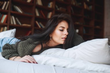 Güzel esmer kadın yeşil kazaklı bir yatağa evde yatıyor