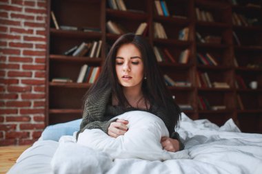 Güzel üzgün esmer kadın yeşil kazaklı bir yatakta yatıyor