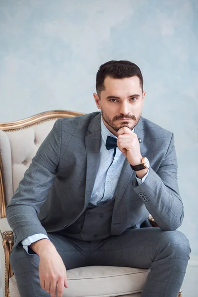 Ritratto di un bellissimo uomo adulto in abito grigio seduto su una sedia in studio. Lo sposo aspetta la sposa. — Foto Stock