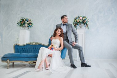 Gelin güzel elbise ve damat gibi beyaz studio iç içeride kanepe evde oturan gri takım elbiseli. Moda düğün tarzı