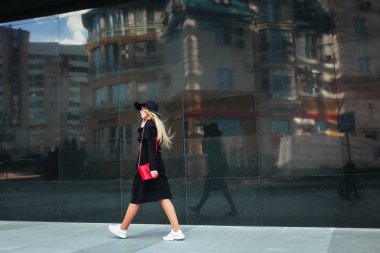 Kırmızı gözlük ve şehirde yürüyüş bir kırmızı çanta giyen güzel genç kadın bir siyah palto ve şapka. Şehrin penceredeki yansıma