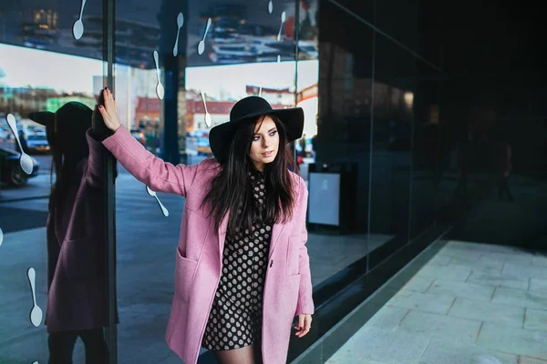 Outdoor portrait of a young beautiful fashionable woman walking on the street. Model wearing stylish pink coat, black hat . Model looking aside. — Stock Photo, Image