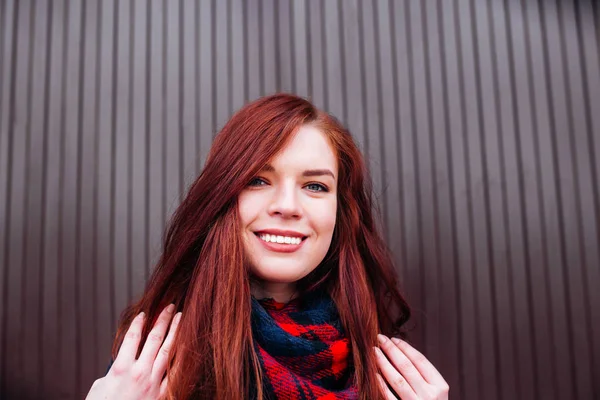 Vista de cerca de la atractiva mujer caucásica feliz con el pelo de jengibre con ropa elegante mirando y sonriendo a la cámara posando contra la pared. Concepto de juventud y felicidad — Foto de Stock