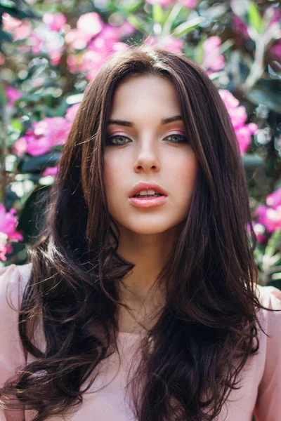 Прекрасне обличчя молодої жінки з макіяжем над рожевими квітами. Портрет досить здорової дівчини зі шкіри. — стокове фото