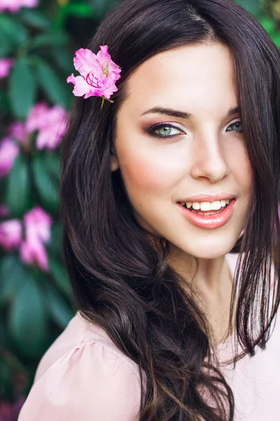 Прекрасне обличчя молодої жінки з макіяжем над рожевими квітами. Портрет досить здорової дівчини зі шкіри. — стокове фото