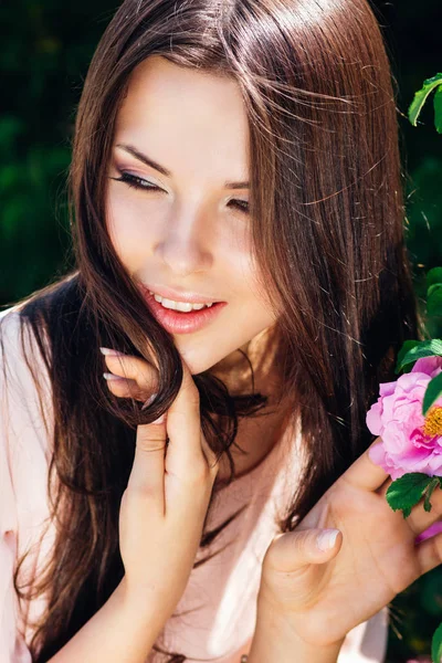 Hermosa joven con el pelo largo y rizado posando cerca de rosas en un jardín. El concepto de publicidad de perfumes . — Foto de Stock