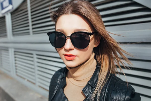 Fashion portrait pretty woman in black rock style in sunglasses over gray background in city